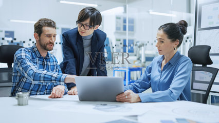 现代工厂办公室会议:女项目经理,亚洲分公司主管与总产品工程师交谈,并向他们展示笔记本电脑屏幕。专业团队解决技术问题照片摄影